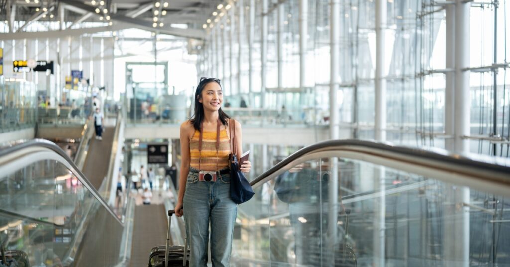 Woman with a suitcase rides an escalator in a modern airport terminal, smiling as she travels