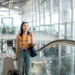 Woman with a suitcase rides an escalator in a modern airport terminal, smiling as she travels