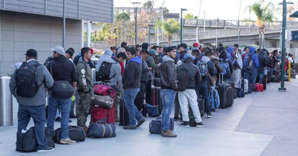 People queue outside a transport terminal, standing with suitcases and travel bags