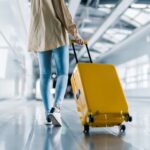 Traveller pulls a yellow suitcase through an airport terminal on a moving walkway