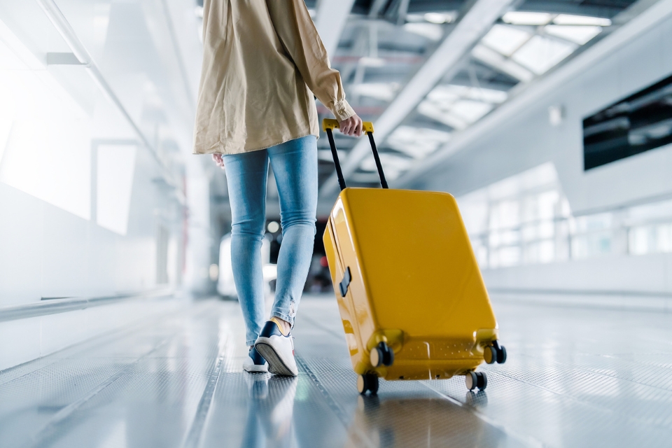 Traveller pulls a yellow suitcase through an airport terminal on a moving walkway