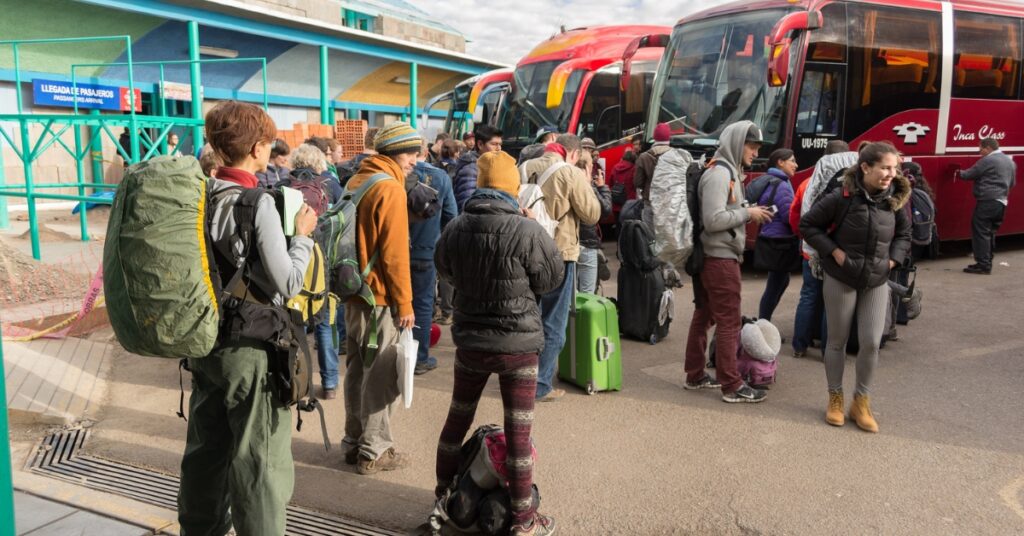 Travellers with backpacks and luggage queue to board coaches at a bus terminal