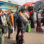 Travellers with backpacks and luggage queue to board coaches at a bus terminal