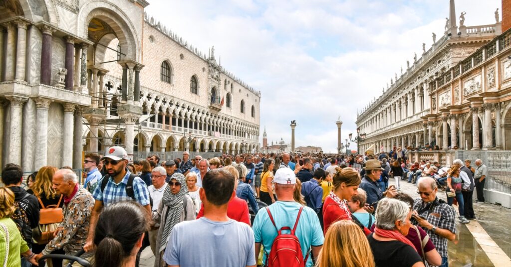 Crowds of tourists fill Venice’s Piazza San Marco between ornate historic buildings under a cloudy sky