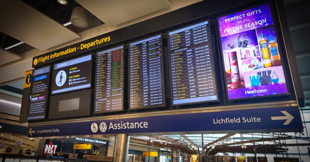 Airport departure information boards display flight schedules and gate details above a terminal concourse