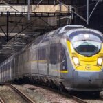 Eurostar high-speed train approaches a station platform beneath overhead power lines