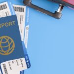 Passport with boarding passes beside a suitcase and model aeroplane on a blue background, representing air travel