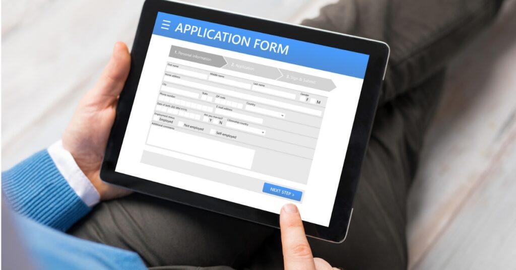 Person completing an online application form on a tablet, with a finger selecting the next step