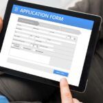 Person completing an online application form on a tablet, with a finger selecting the next step