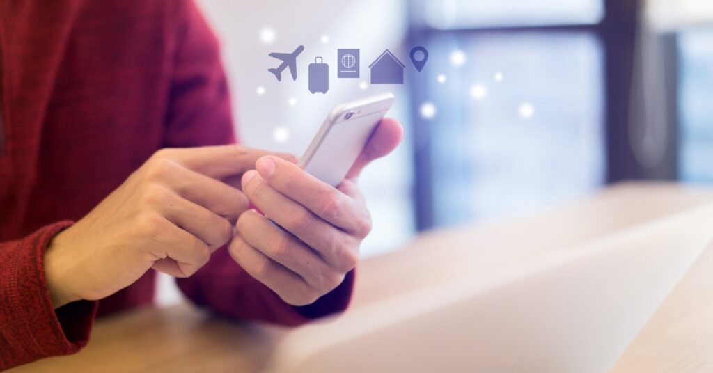 Person using a smartphone with travel icons for flights, luggage, passport and accommodation floating above the screen
