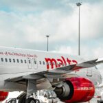 Air Malta aircraft parked on the airport tarmac beneath a cloudy sky, with ground service equipment nearby