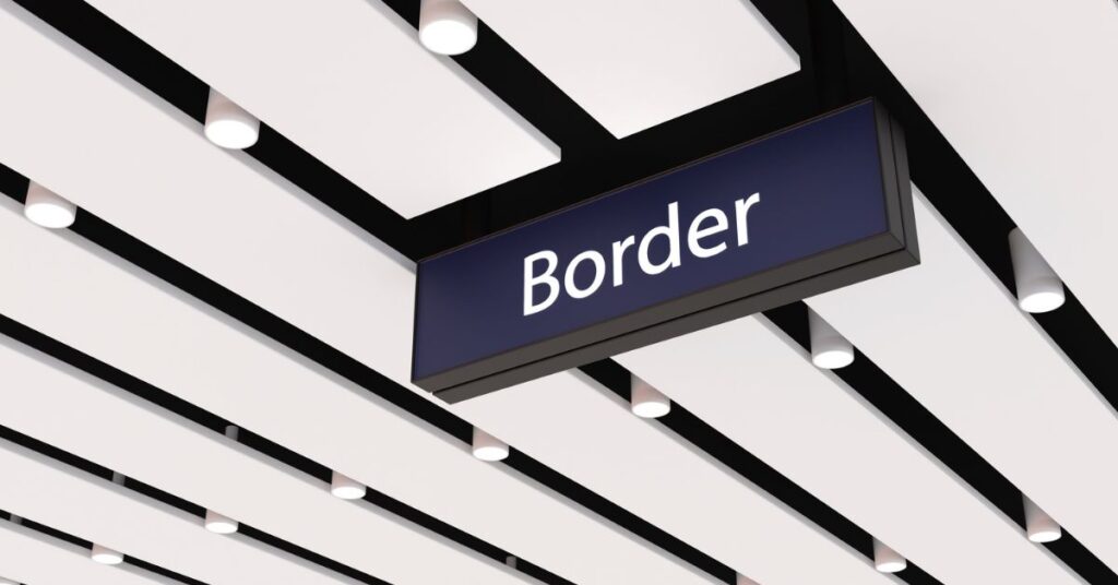 Hanging Border sign beneath a modern airport ceiling with white panels and spotlights