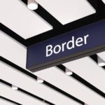 Hanging Border sign beneath a modern airport ceiling with white panels and spotlights