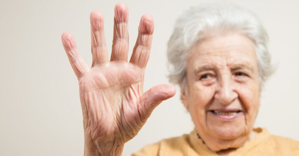 Smiling elderly woman raises an open hand towards the camera