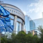European Union flags flying outside a modern institutional building on a sunny day