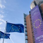 European Union flags fly outside a modern building displaying a purple ‘United for our Future’ banner