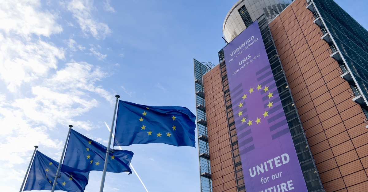 European Union flags fly outside a modern building displaying a purple ‘United for our Future’ banner