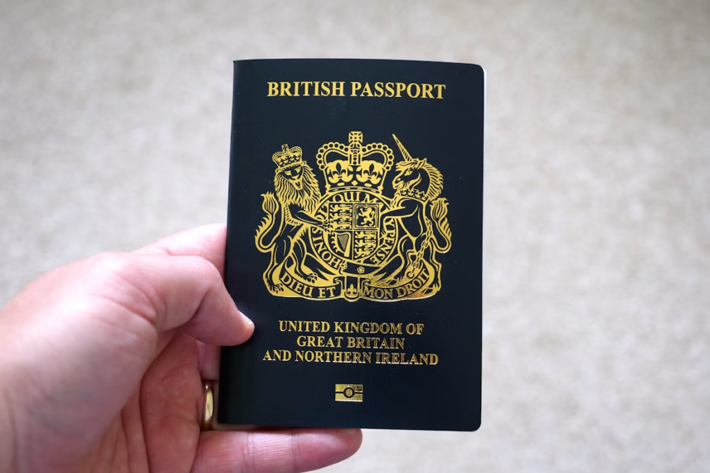 Hand holding a British passport with the UK coat of arms displayed on the cover