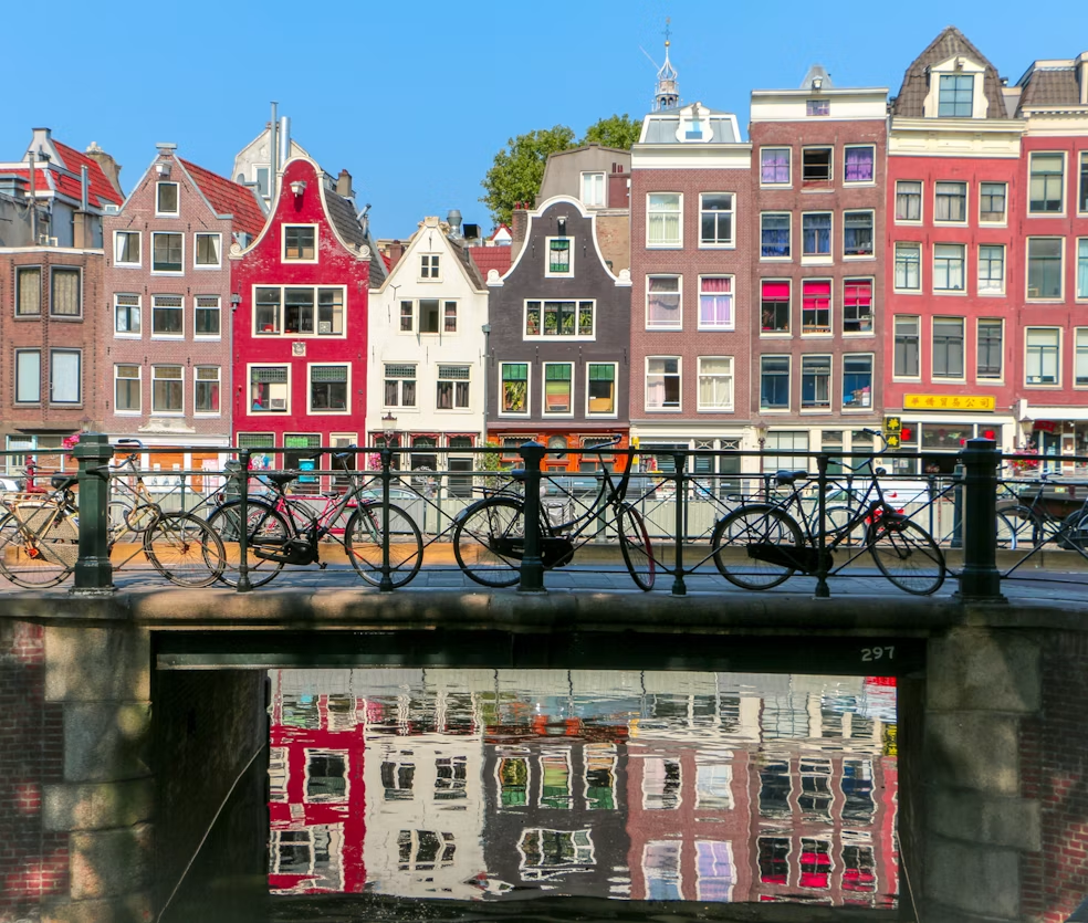 Traditional canal houses and bicycles line a bridge in Amsterdam, reflected in the calm canal below
