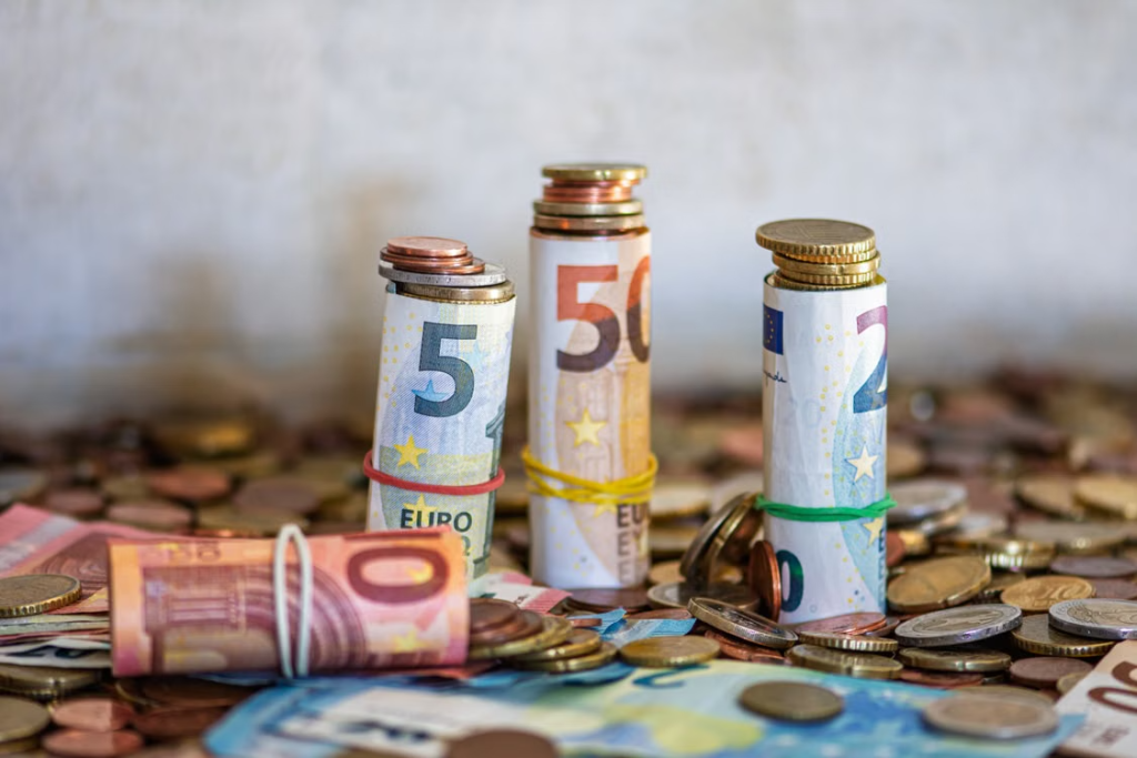 Rolled euro banknotes and stacks of coins are arranged among scattered European currency
