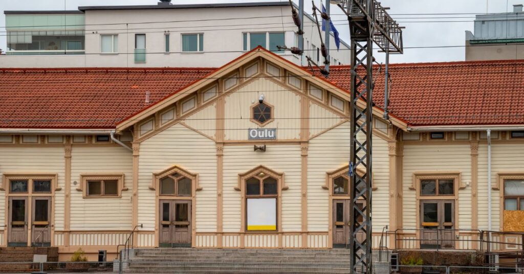 Historic Oulu railway station with a cream timber façade, red tiled roof and overhead power lines