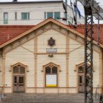Historic Oulu railway station with a cream timber façade, red tiled roof and overhead power lines