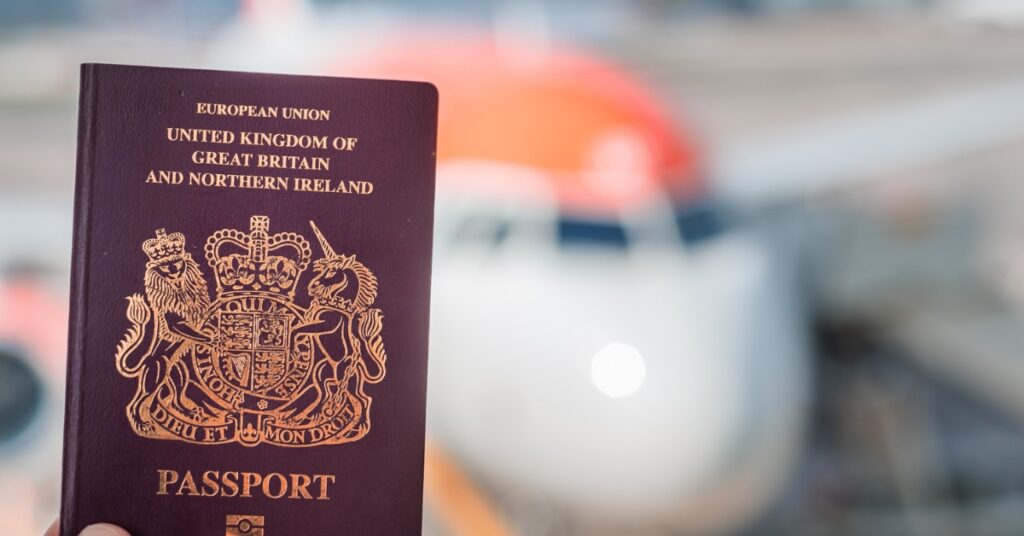 British passport held in front of a blurred passenger aircraft at an airport