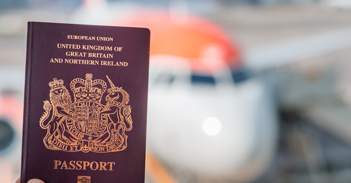 British passport held in front of a blurred passenger aircraft at an airport