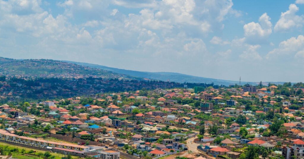 Hilly cityscape with red-roofed homes and green neighbourhoods beneath a bright, cloud-filled sky