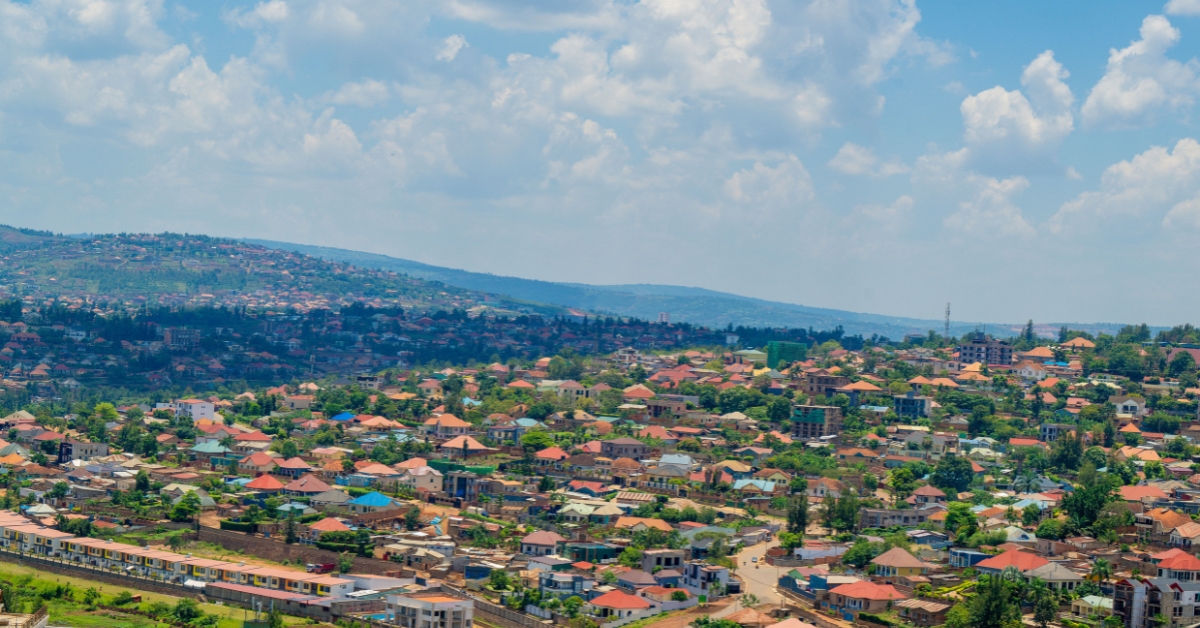 Hilly cityscape with red-roofed homes and green neighbourhoods beneath a bright, cloud-filled sky
