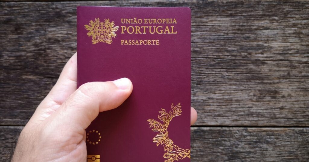 Hand holding a Portuguese passport over a dark wooden surface