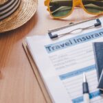 Travel insurance form with passports, sunglasses, a sun hat and a toy plane on a wooden table