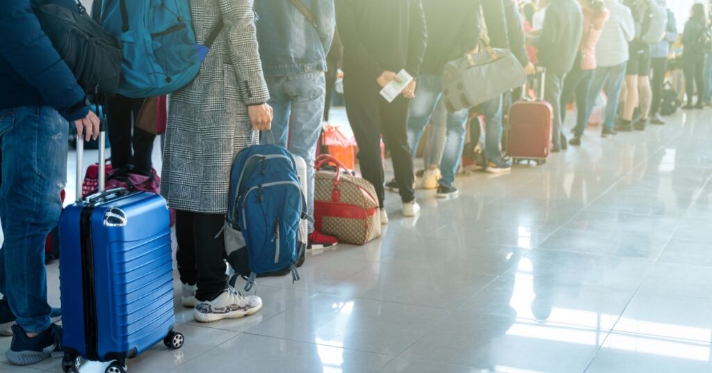 Travellers queue with suitcases and backpacks inside a bright airport terminal