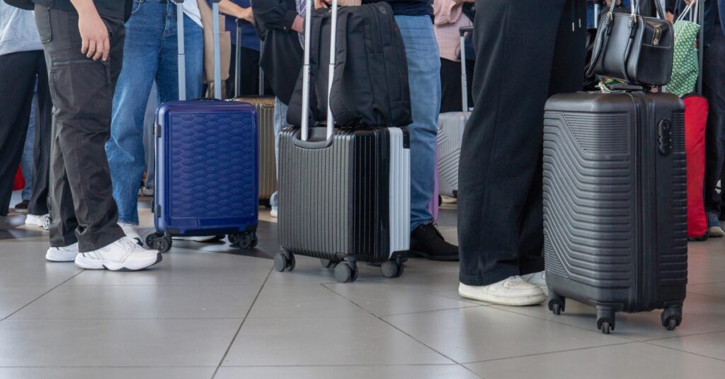 Travellers stand with wheeled suitcases in a crowded airport terminal