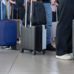 Travellers stand with wheeled suitcases in a crowded airport terminal