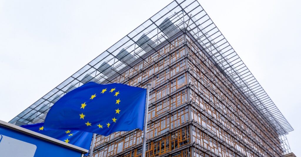 European Union flag waving outside the modern glass-fronted Council of the European Union building in Brussels
