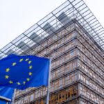 European Union flag waving outside the modern glass-fronted Council of the European Union building in Brussels
