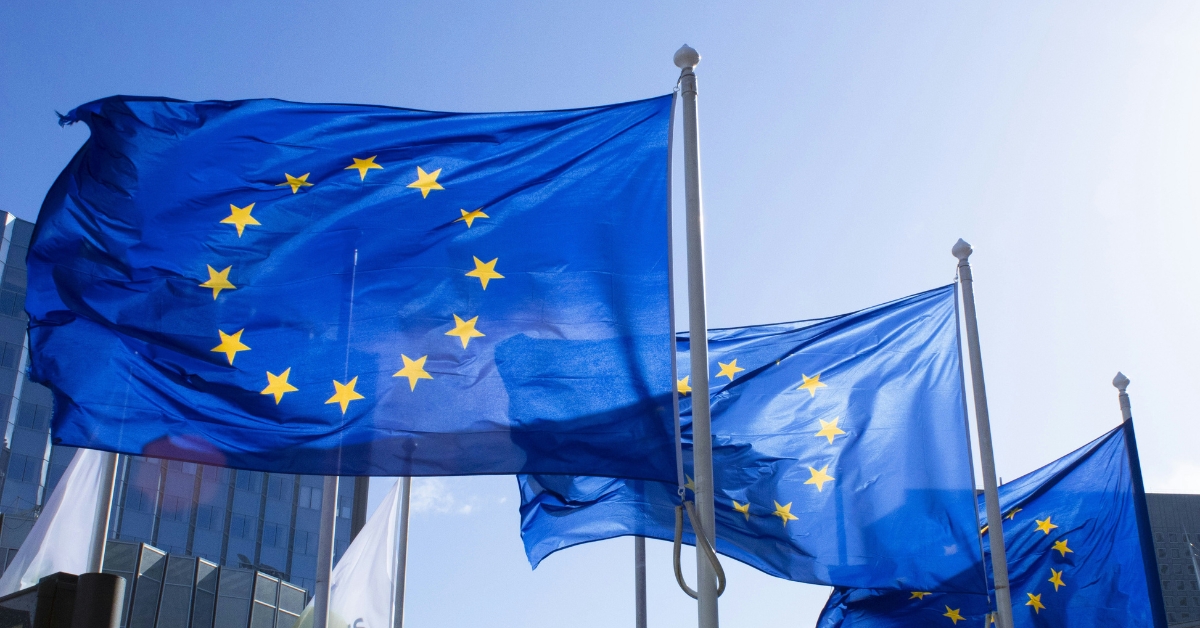 European Union flags waving on flagpoles outside modern buildings under a clear blue sky
