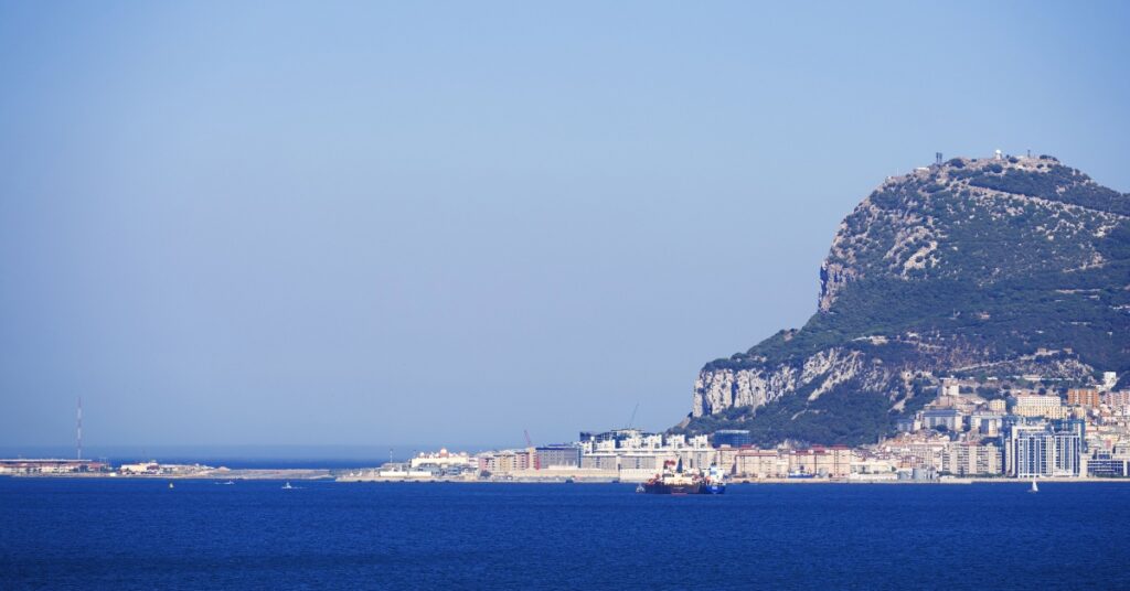 The Rock of Gibraltar rises above the coastline and deep blue Mediterranean Sea under a clear sky