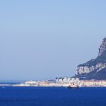 The Rock of Gibraltar rises above the coastline and deep blue Mediterranean Sea under a clear sky