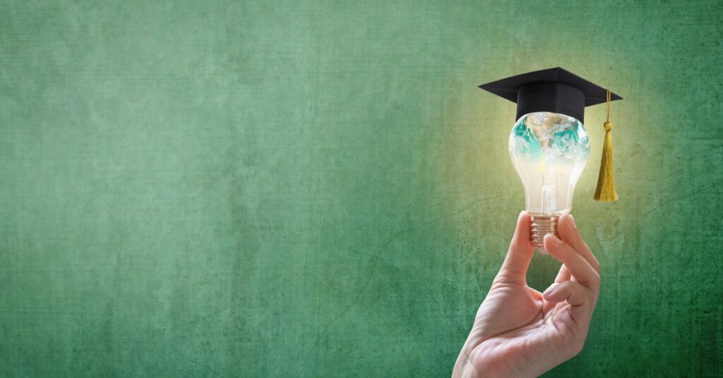 Hand holding a light bulb shaped like a globe and topped with a graduation cap against a green background