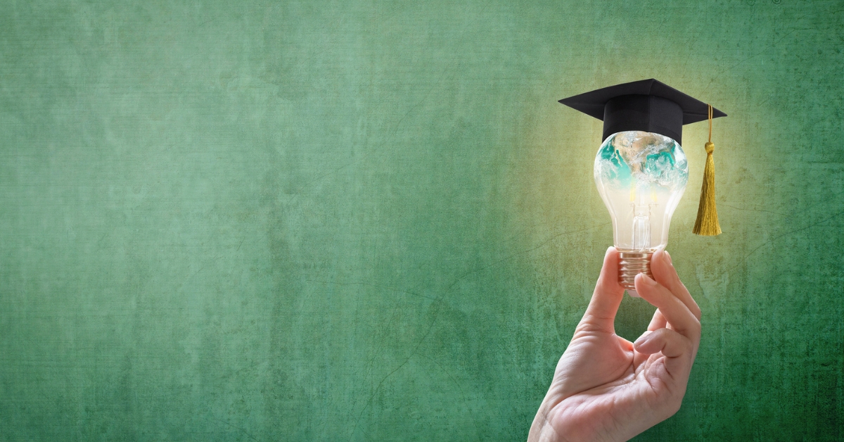 Hand holding a light bulb shaped like a globe and topped with a graduation cap against a green background