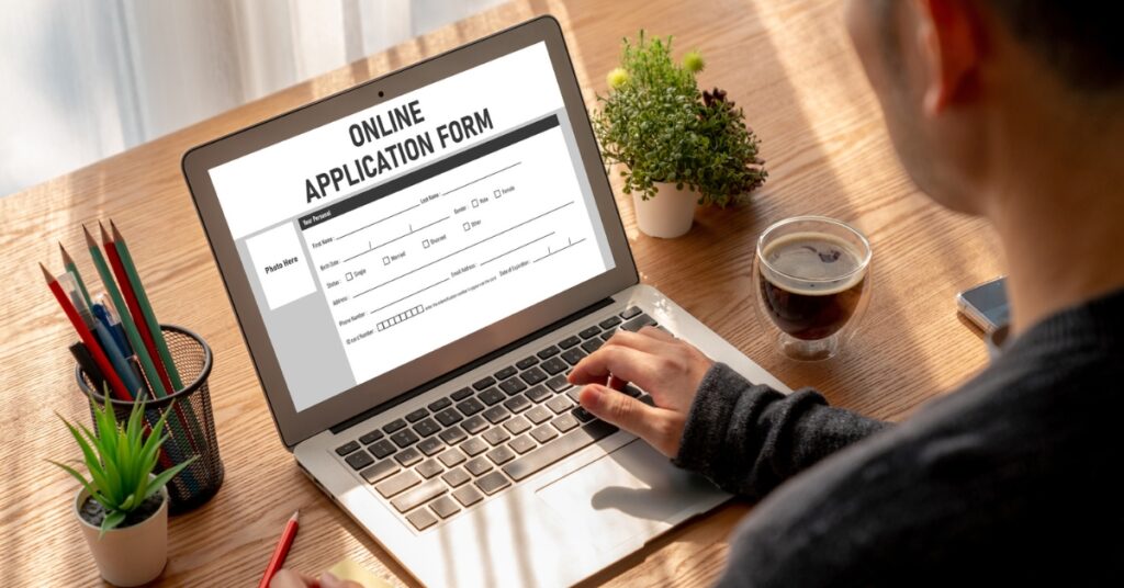 Person filling out an online application form on a laptop at a wooden desk