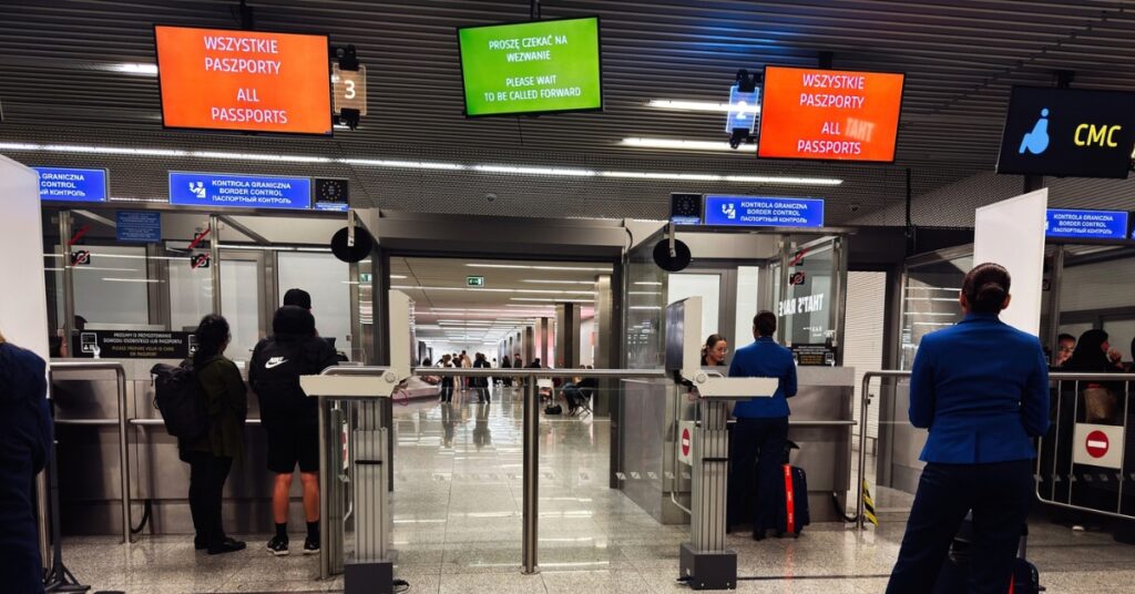 Travellers queue at airport border control beneath ‘All Passports’ signs in Polish and English