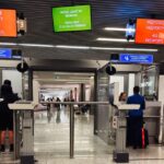 Travellers queue at airport border control beneath ‘All Passports’ signs in Polish and English