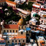 Aerial view of a domed church surrounded by colourful hillside buildings in Positano, Italy