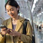 Woman wearing earphones uses a smartphone while standing inside a train