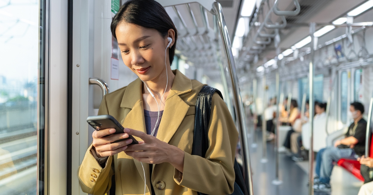 Woman wearing earphones uses a smartphone while standing inside a train